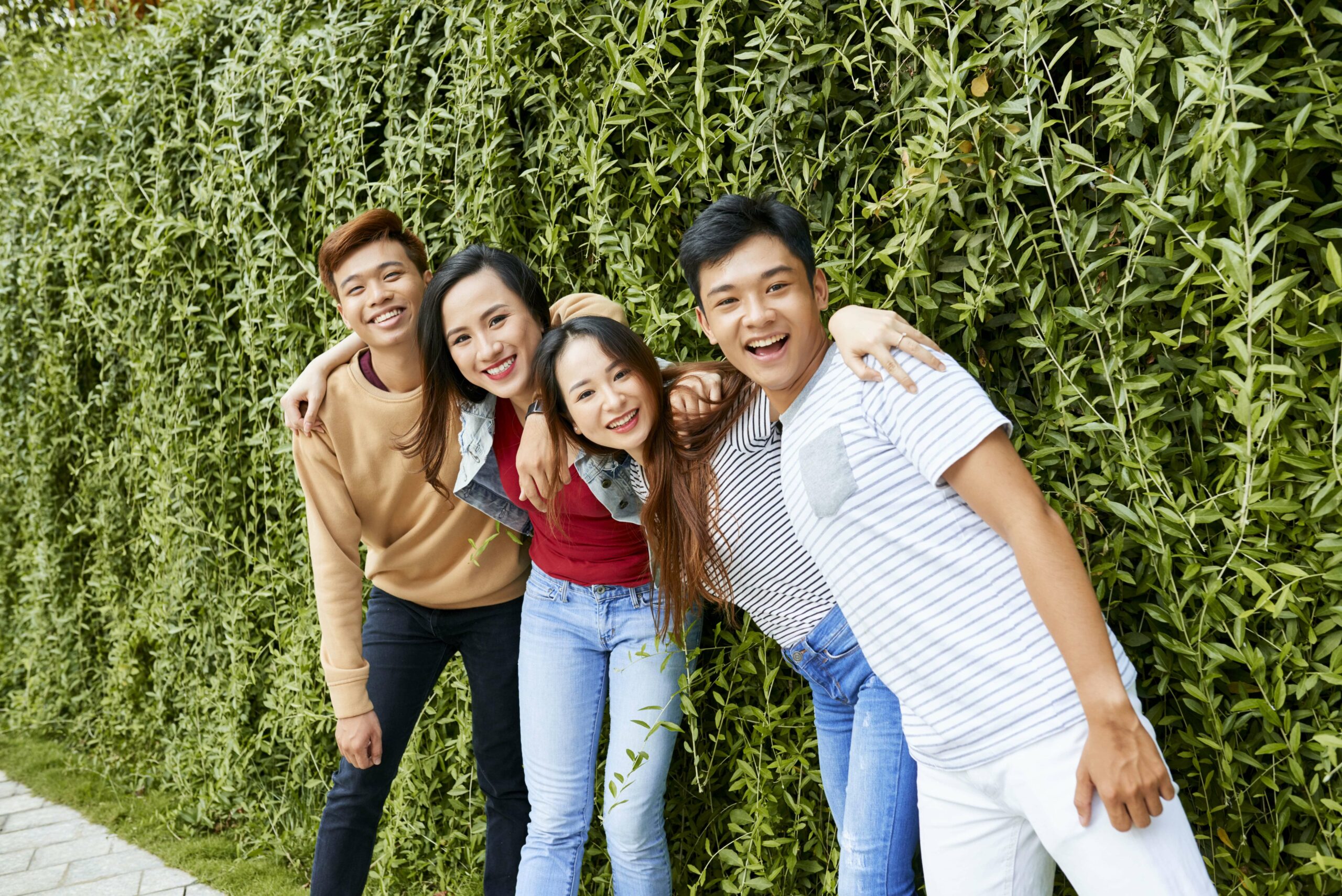 Four Asian Friends in front of a green hedge.